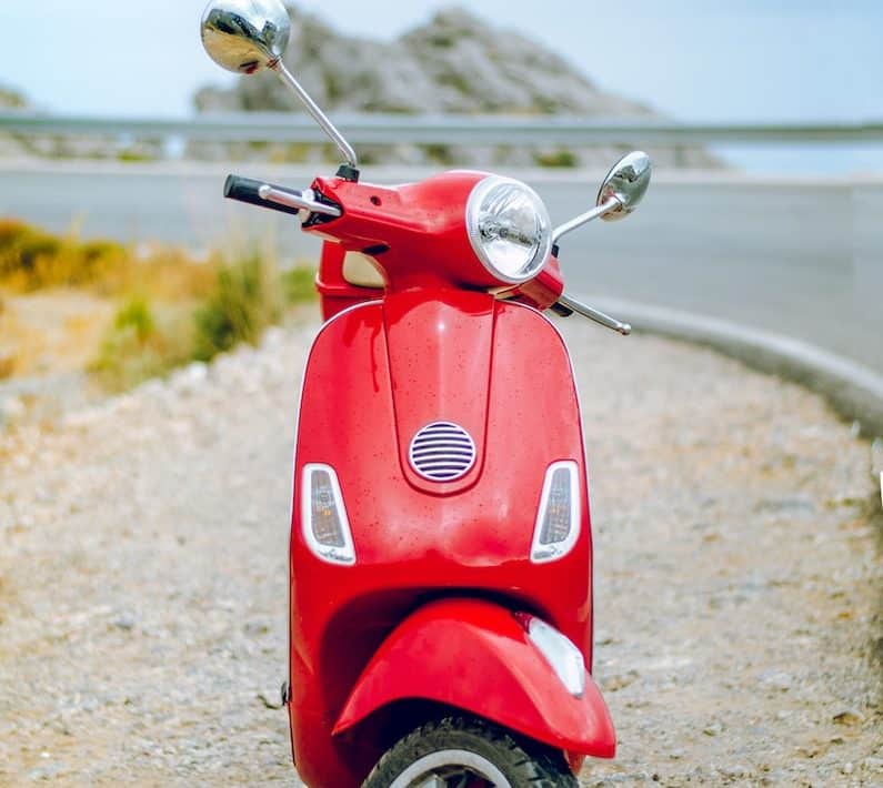red Vespa motor scooter on side of the road