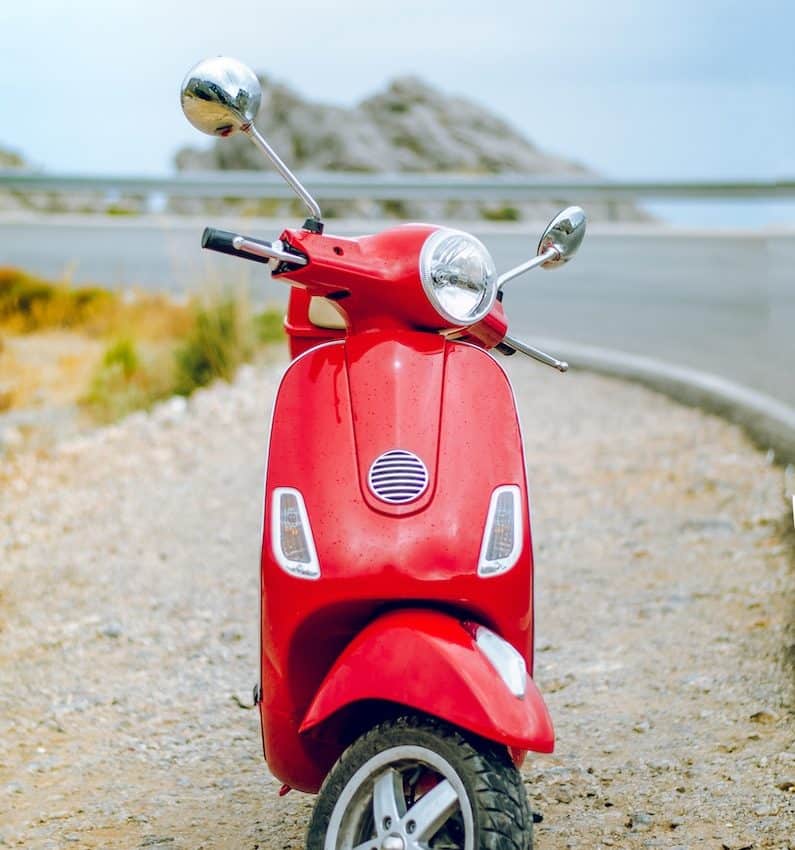 red Vespa motor scooter on side of the road